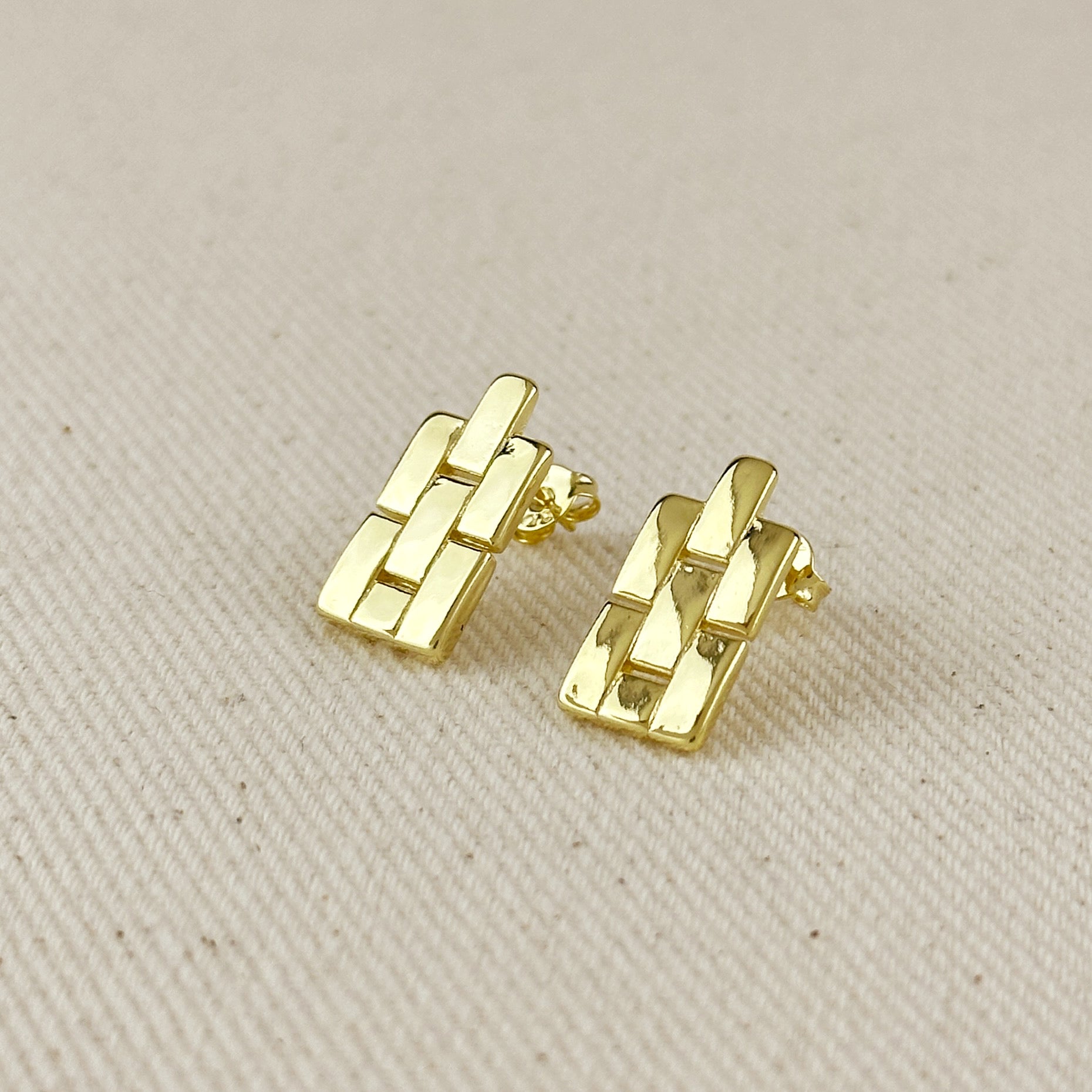 Gold earrings on a beige fabric background