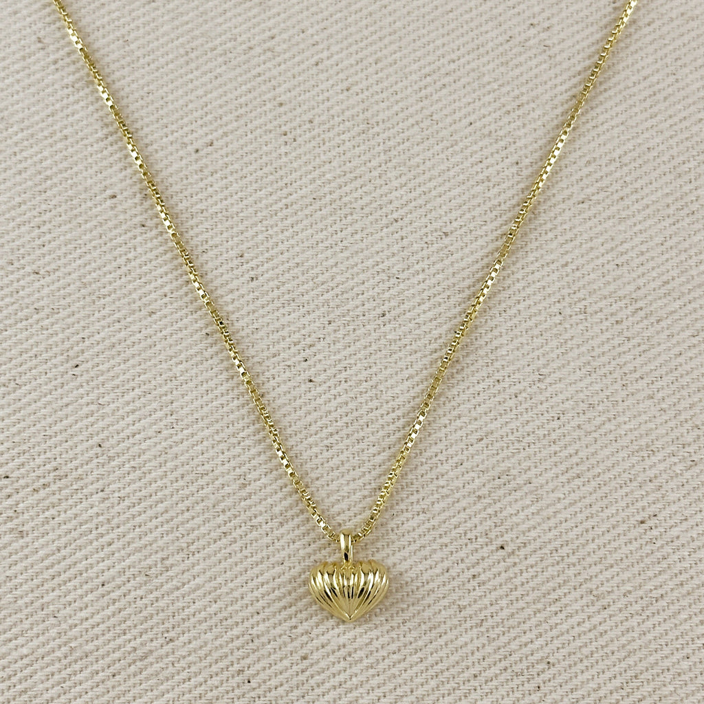 Gold necklace with a heart-shaped pendant on a beige fabric background