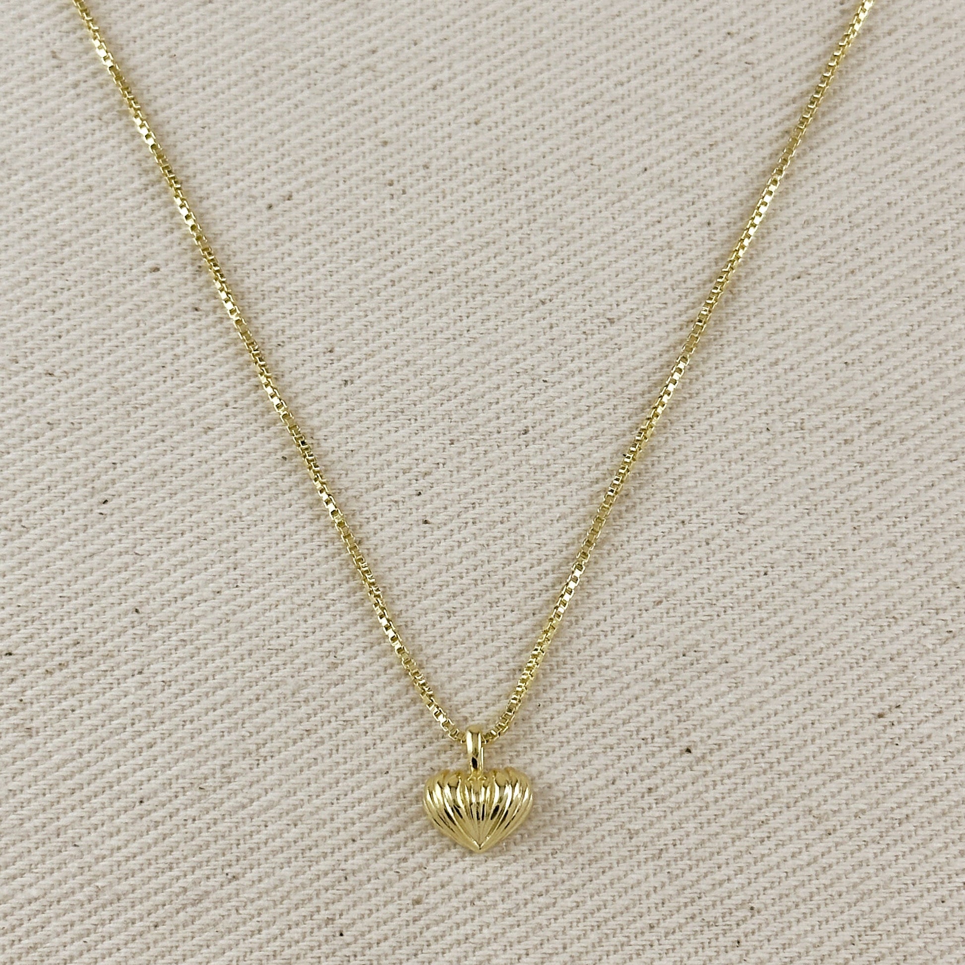 Gold necklace with a heart-shaped pendant on a beige fabric background