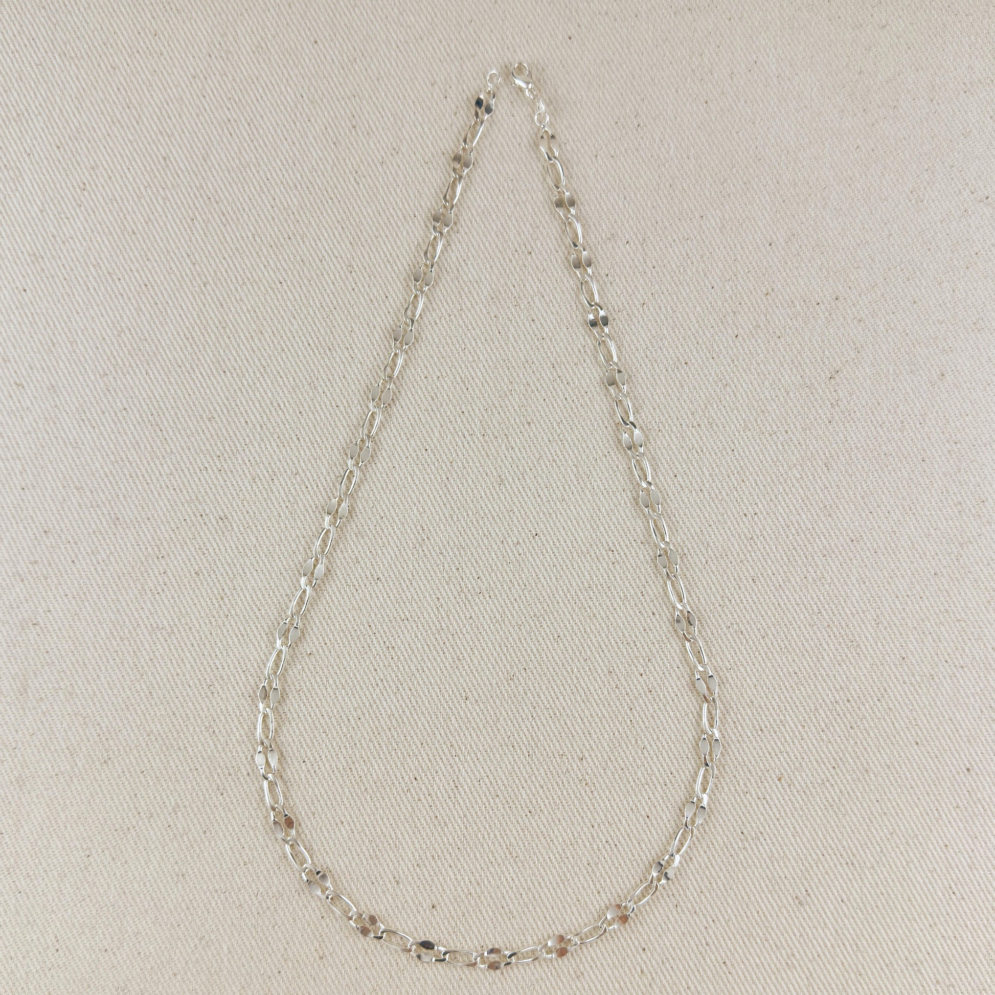 Silver chain necklace on a light beige fabric background