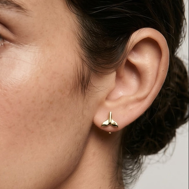 Close-up of a person wearing gold earrings with a neutral background