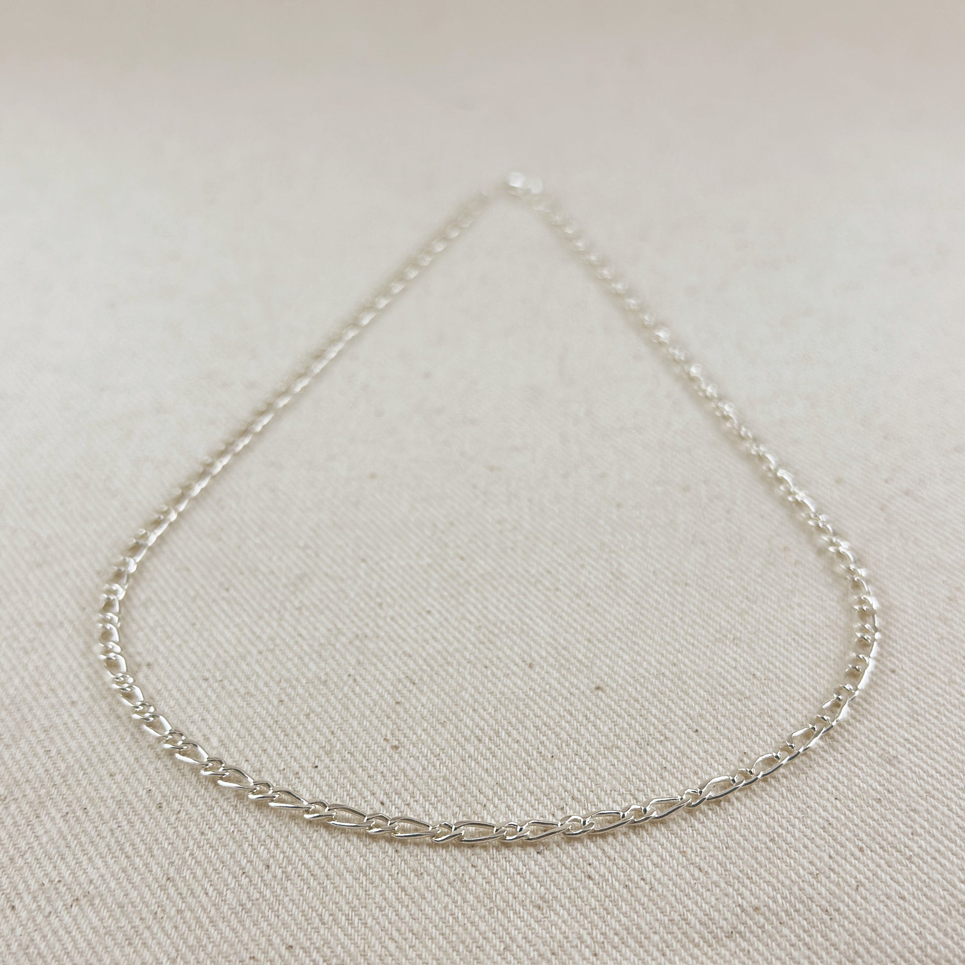 Silver chain necklace on a light beige fabric background