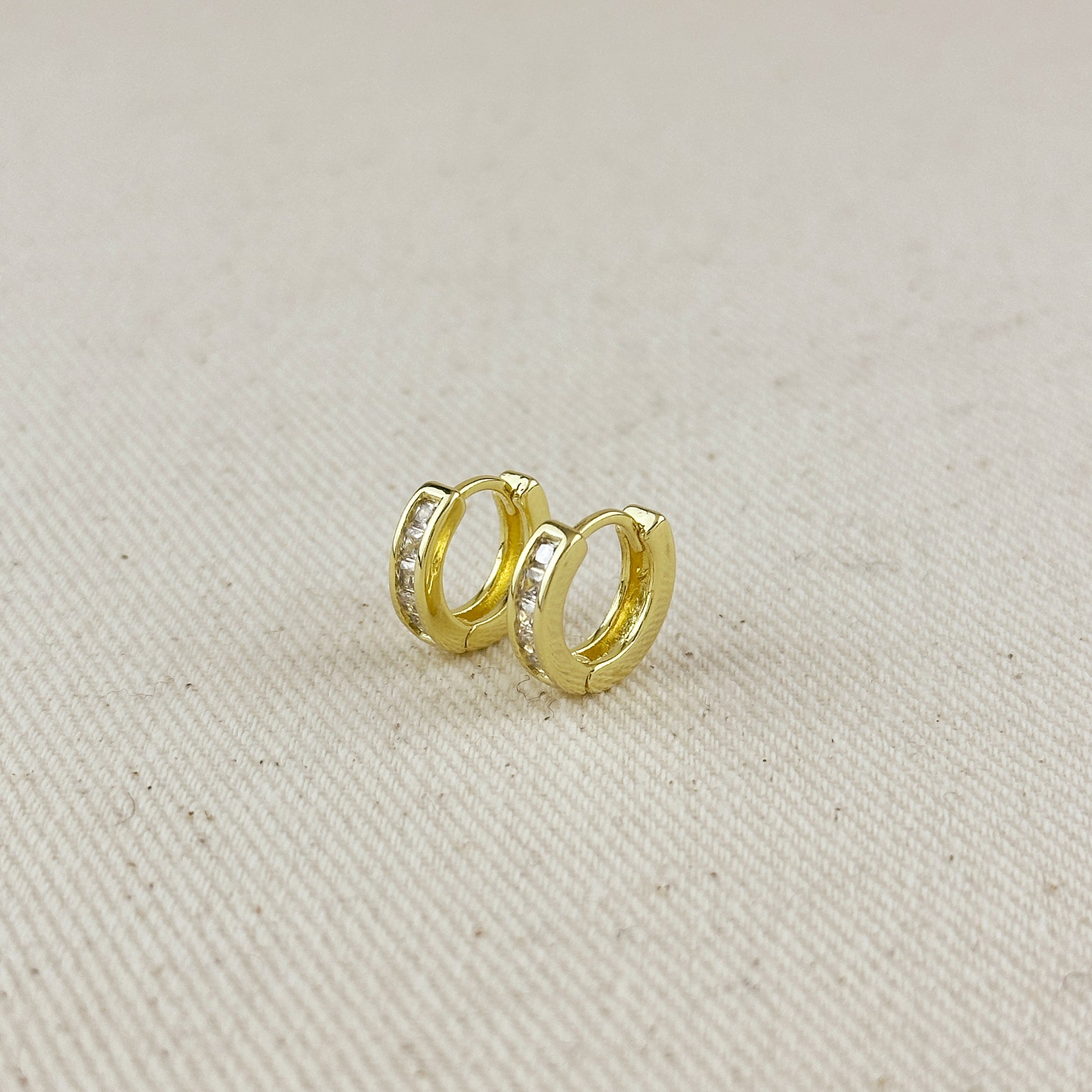 Gold hoop earrings with embedded stones on a beige fabric background