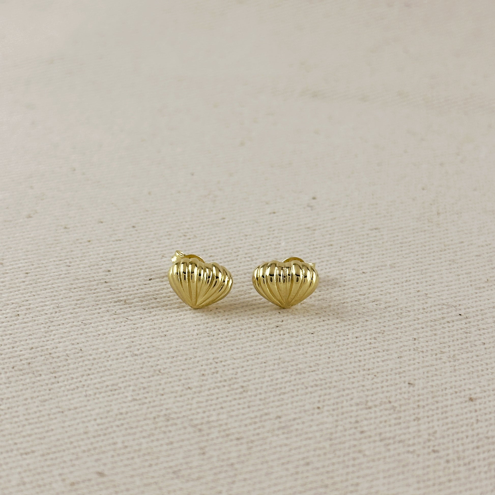 Gold heart-shaped earrings on a beige fabric background