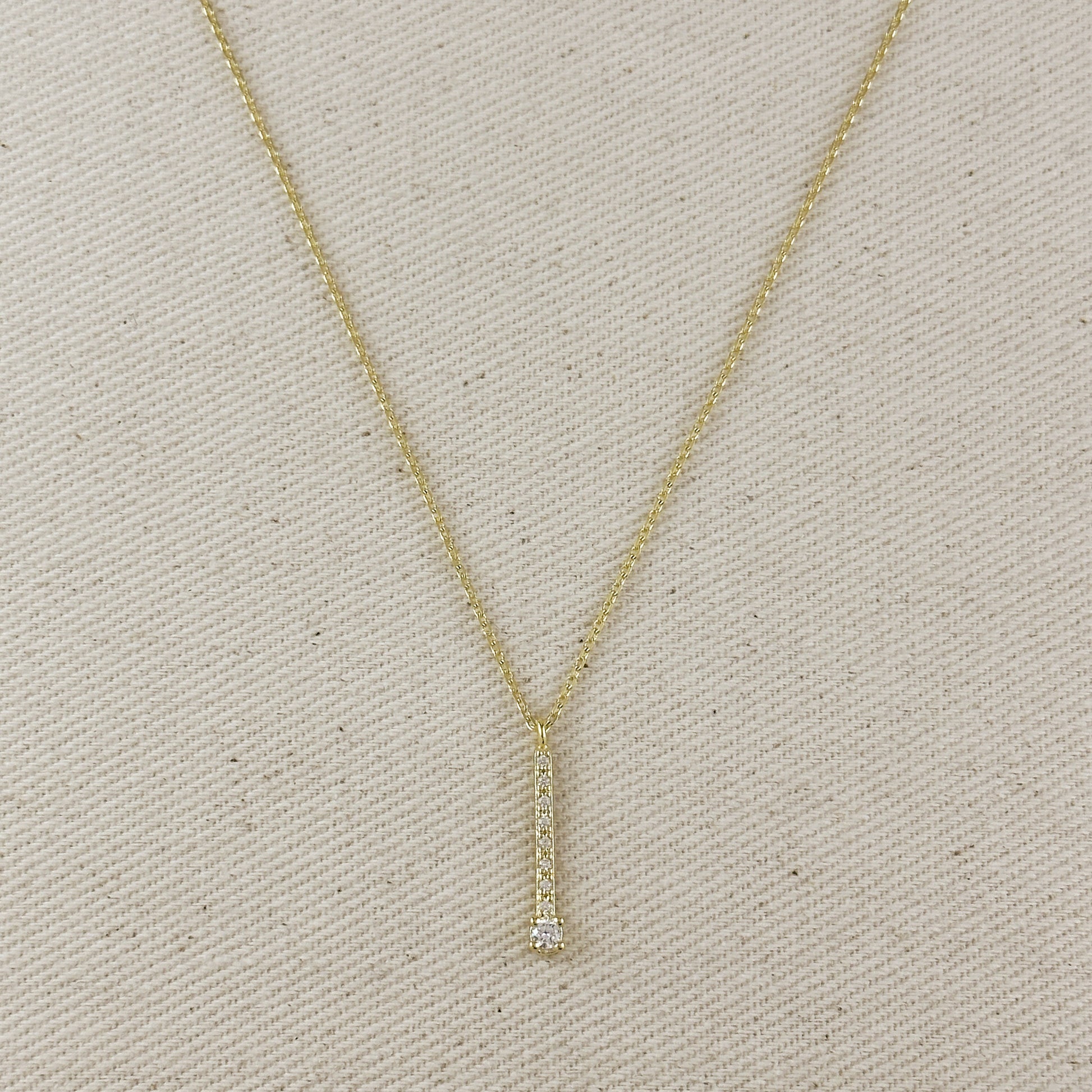 Gold necklace with a small diamond pendant on a beige fabric background