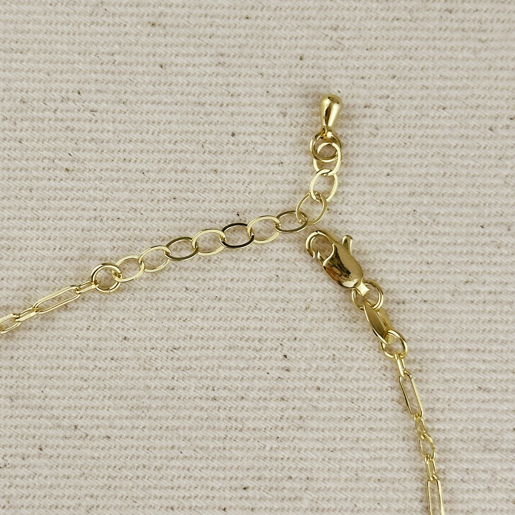 Close-up of 18k gold filled paperclip chain anchor with clasp detail on fabric background.