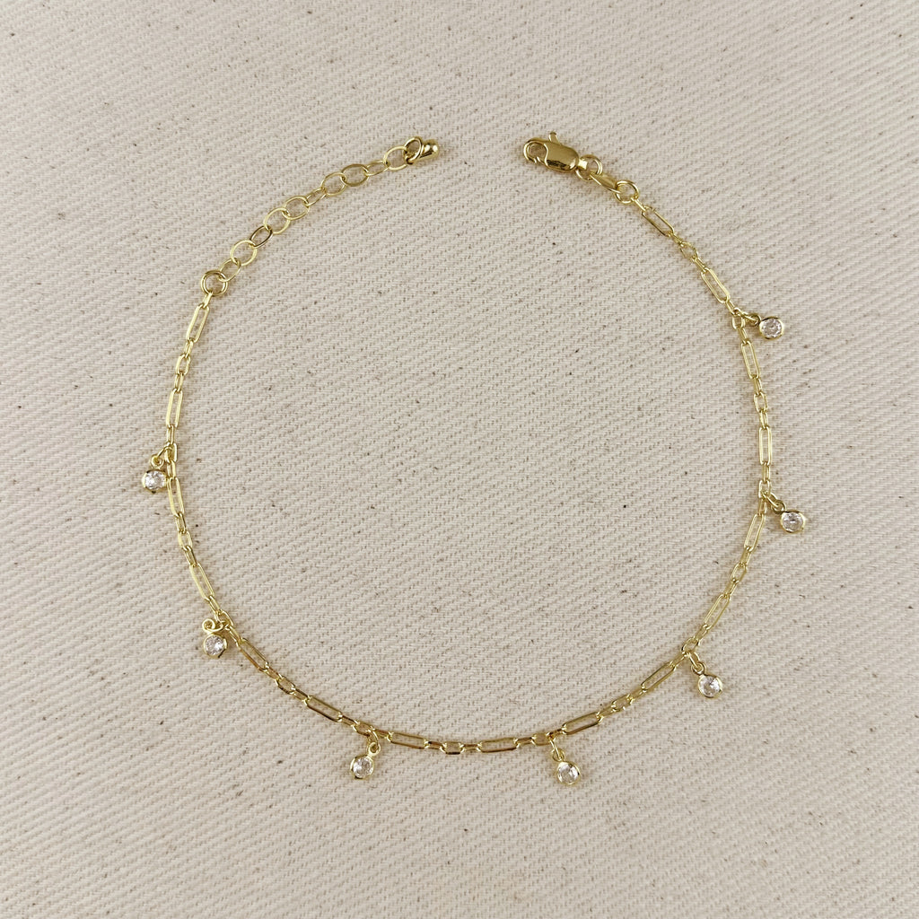 Gold anklet with small dangling charms on a beige fabric background