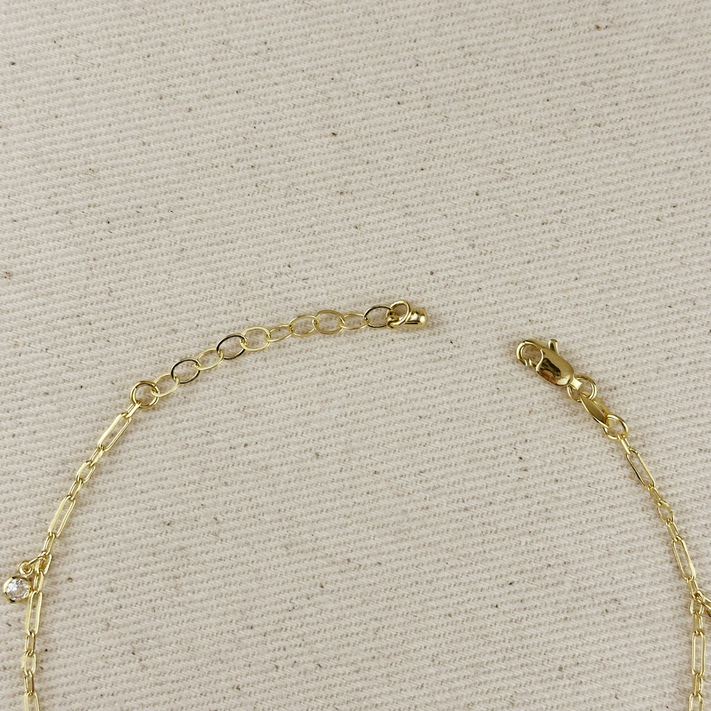 Close-up of 18K gold filled paperclip chain anklet, showcasing clasp and CZ drop detail on textured fabric background.