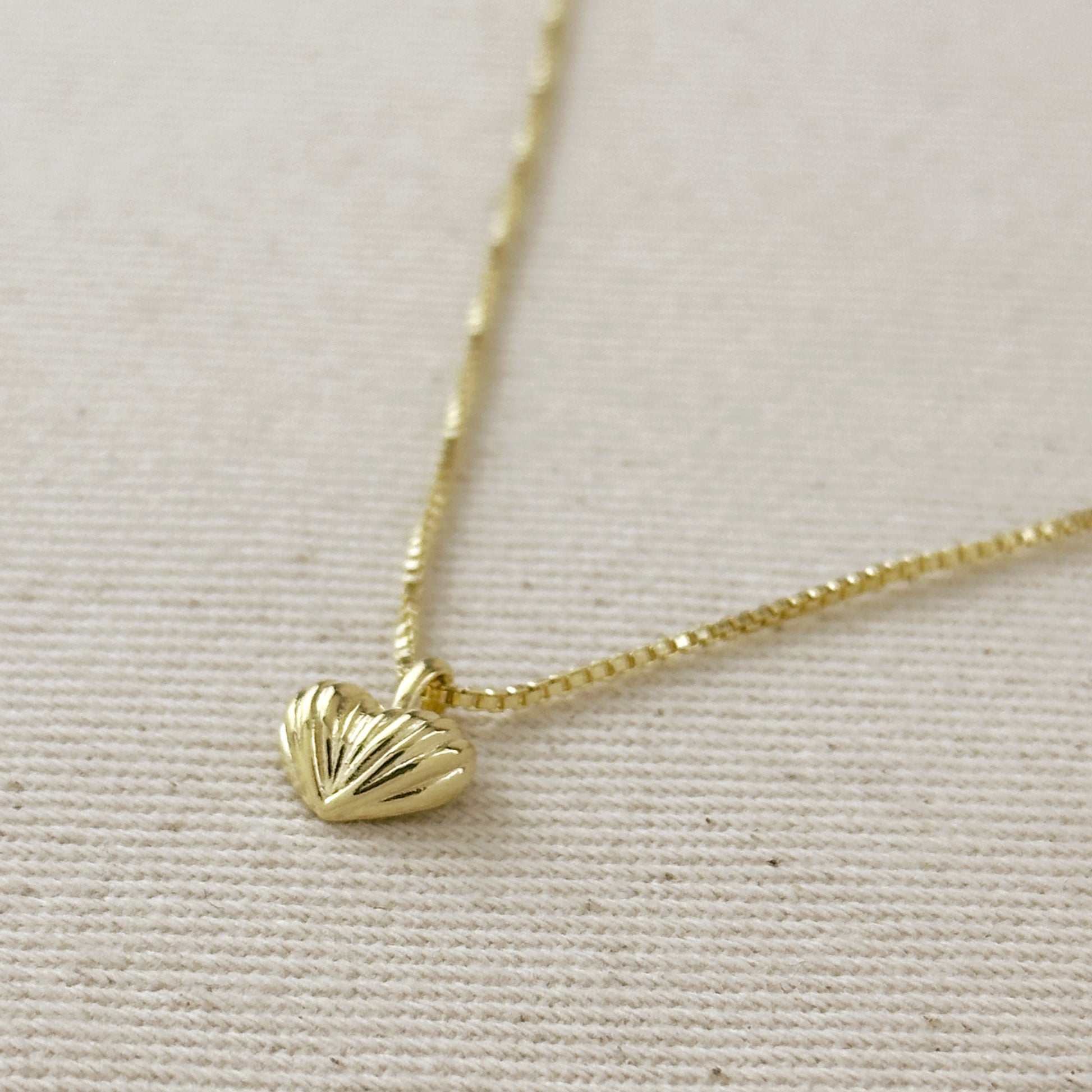 Gold necklace with a heart-shaped pendant on a light beige background