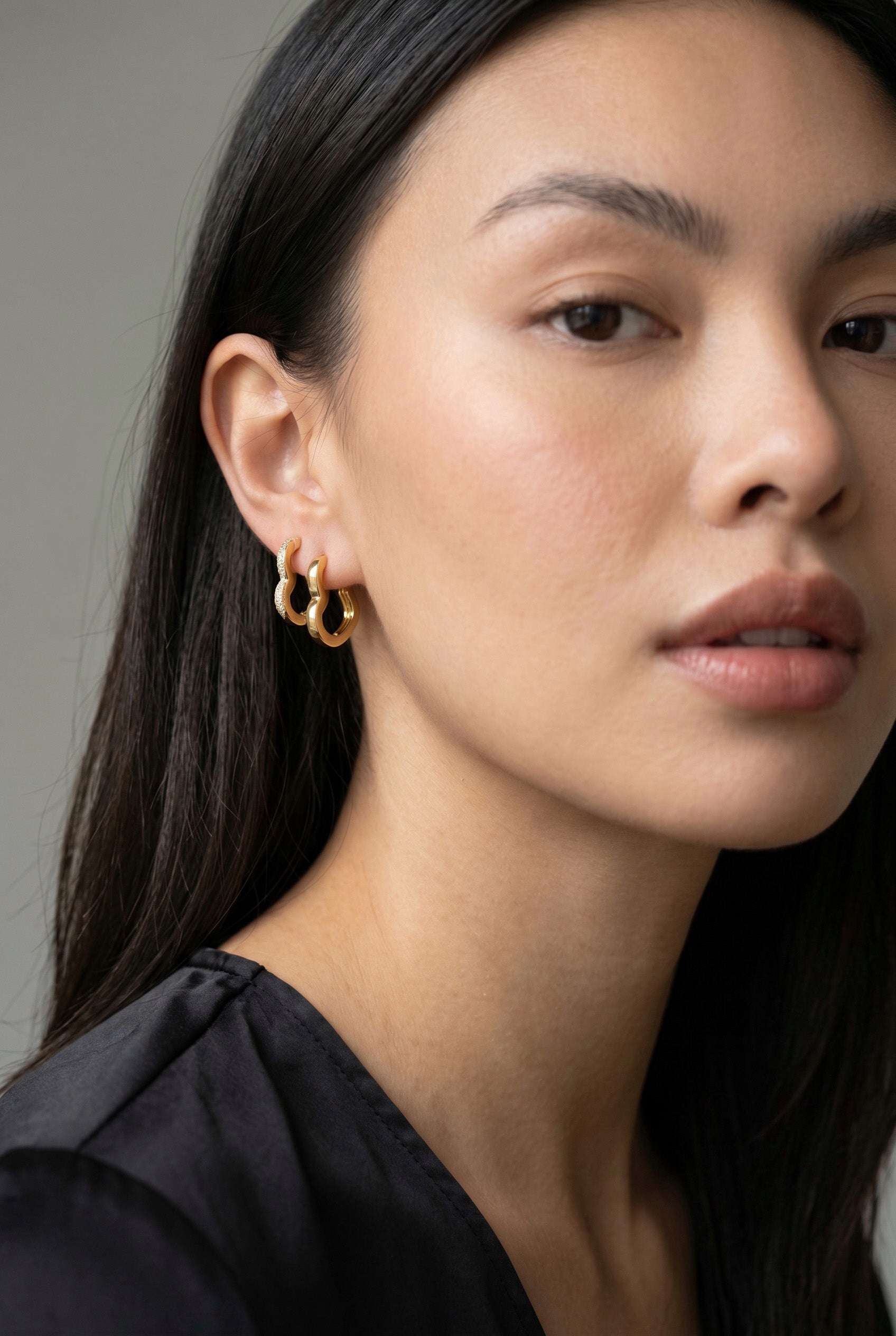 Close-up of a person wearing gold hoop earrings with a neutral background