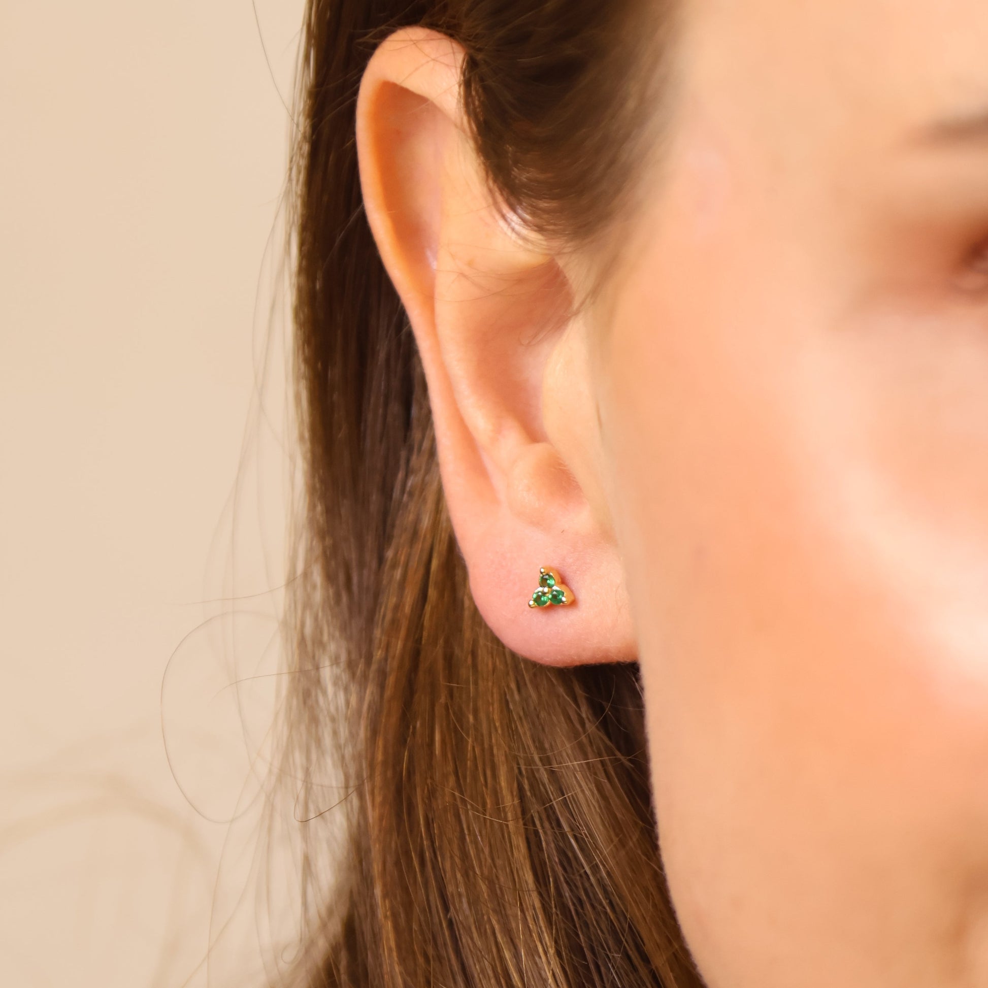 Close-up of a person wearing a green earring with a neutral background