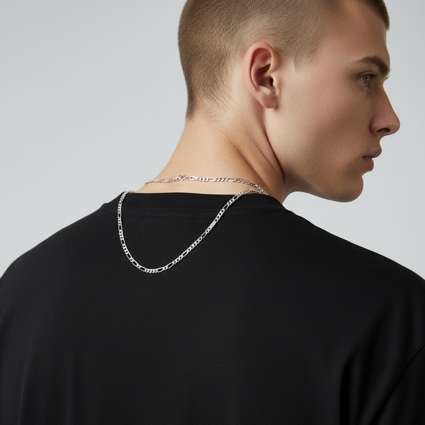 Man wearing a black shirt with a silver chain necklace on a plain background