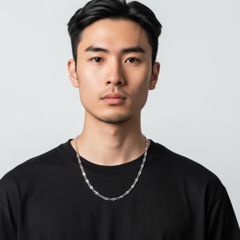 Man wearing a black t-shirt and silver chain necklace against a light gray background