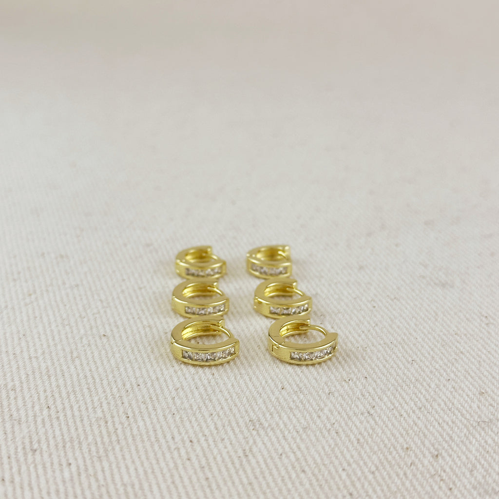Gold hoop earrings with embedded stones on a beige fabric background