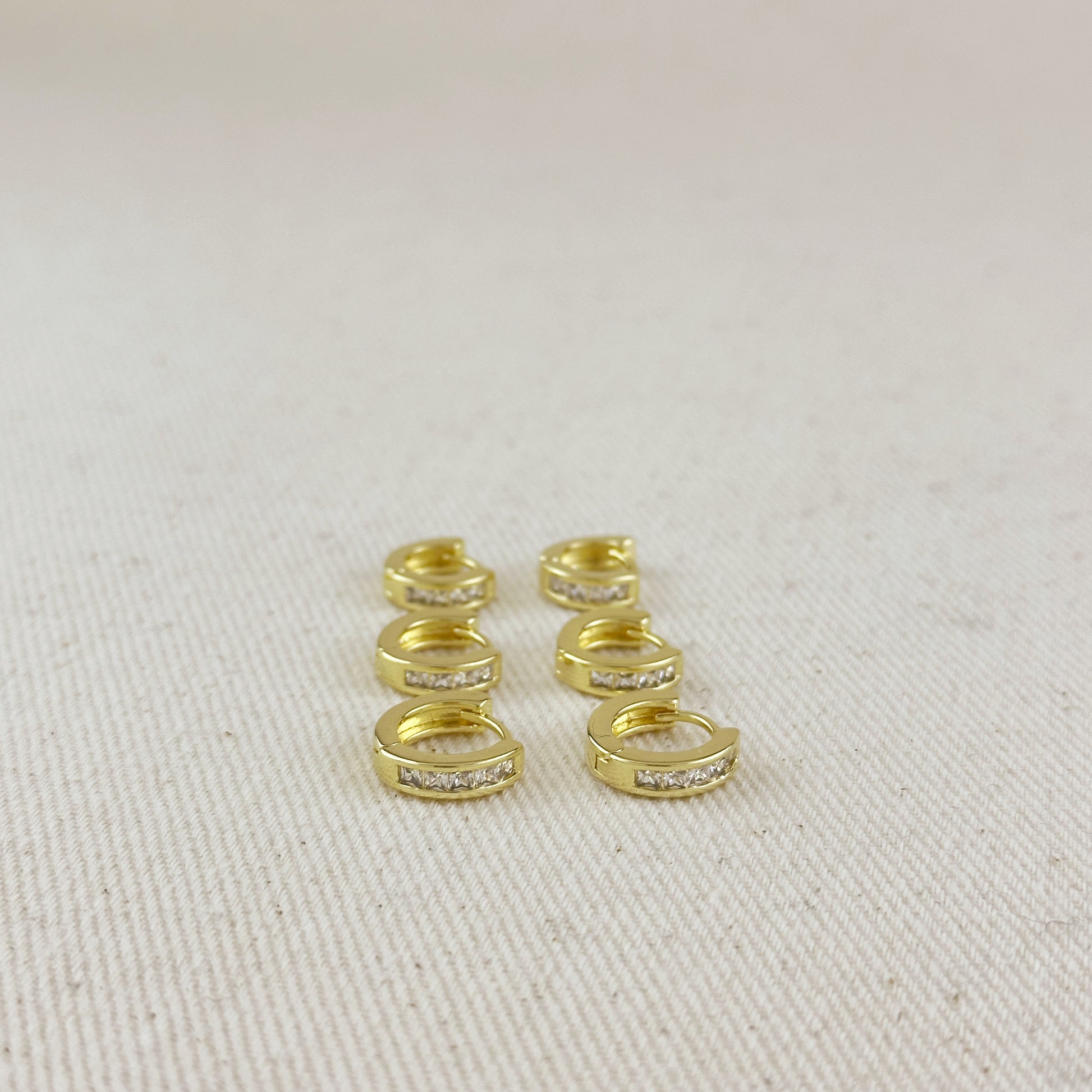 Gold hoop earrings with embedded stones on a beige fabric background