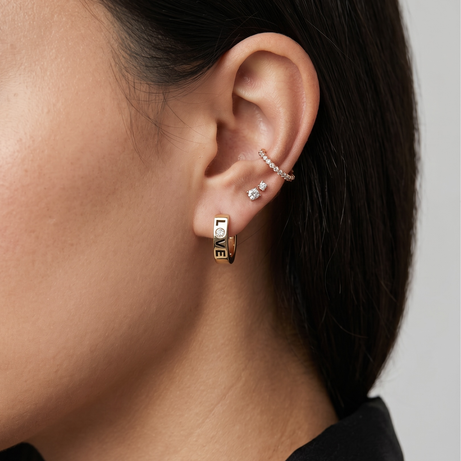 Close-up of a person wearing gold hoop earrings with a neutral background