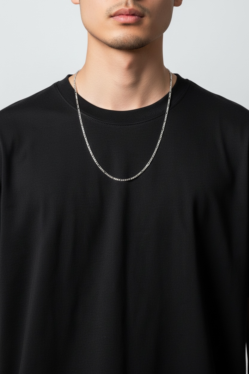 Person wearing a black shirt with a silver chain necklace on a plain background