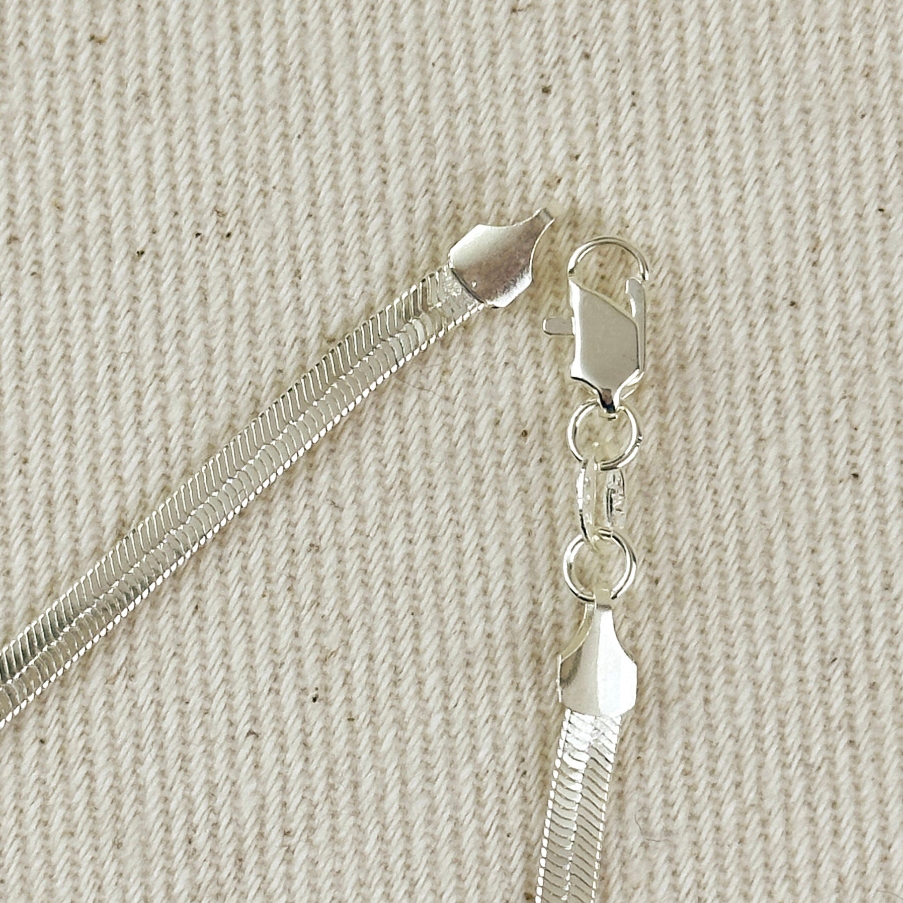 Close-up of a silver chain with clasp on a textured beige background