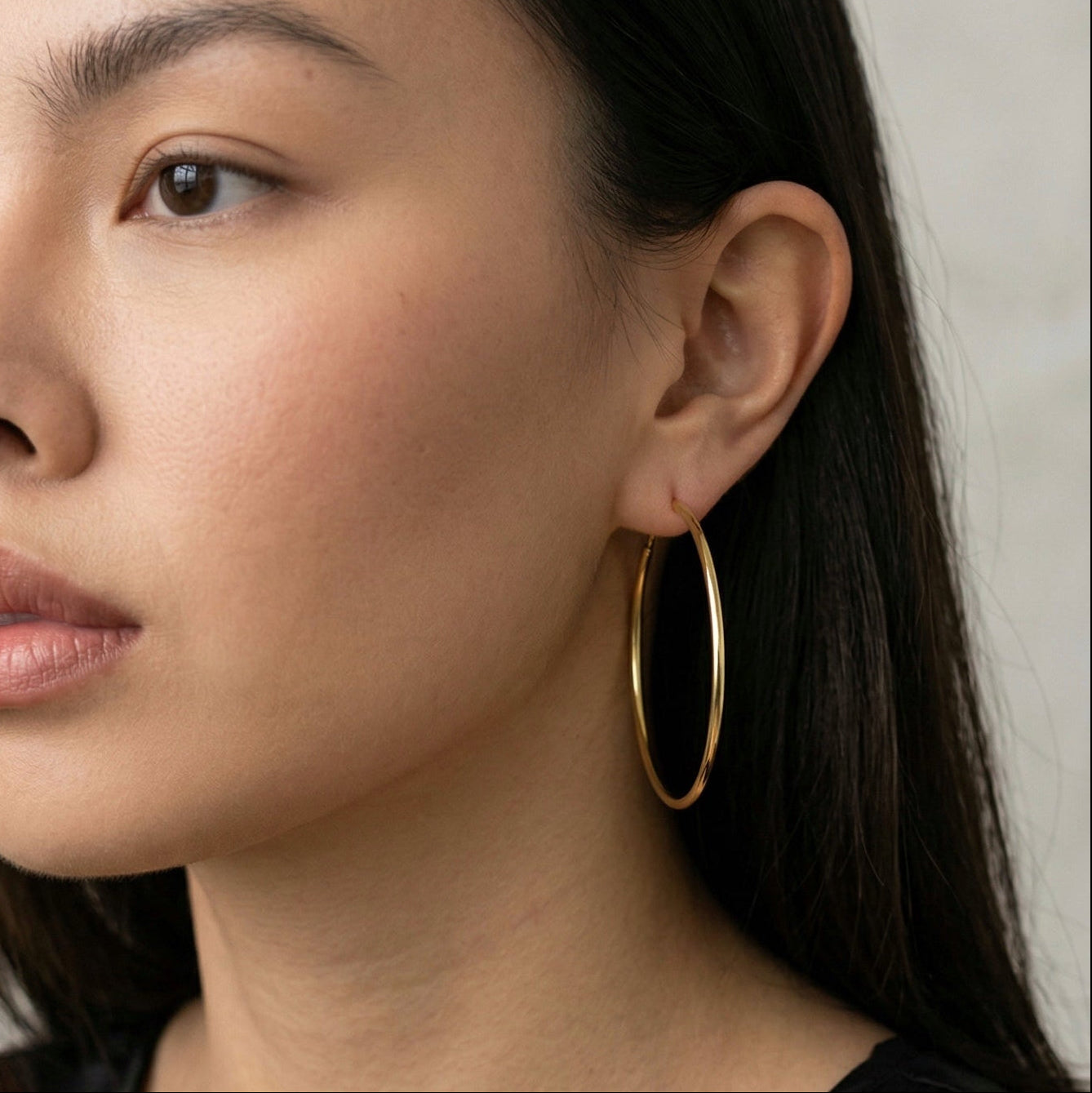 Woman wearing a  40mm gold hoop earring against a neutral background