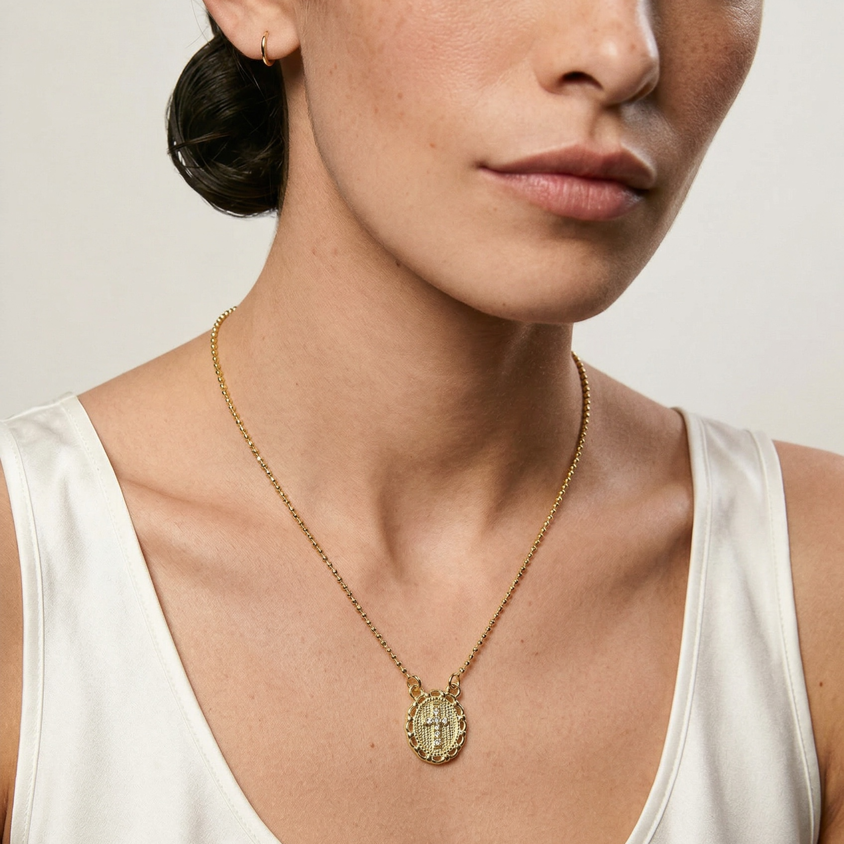 Woman wearing a gold necklace with a pendant against a neutral background