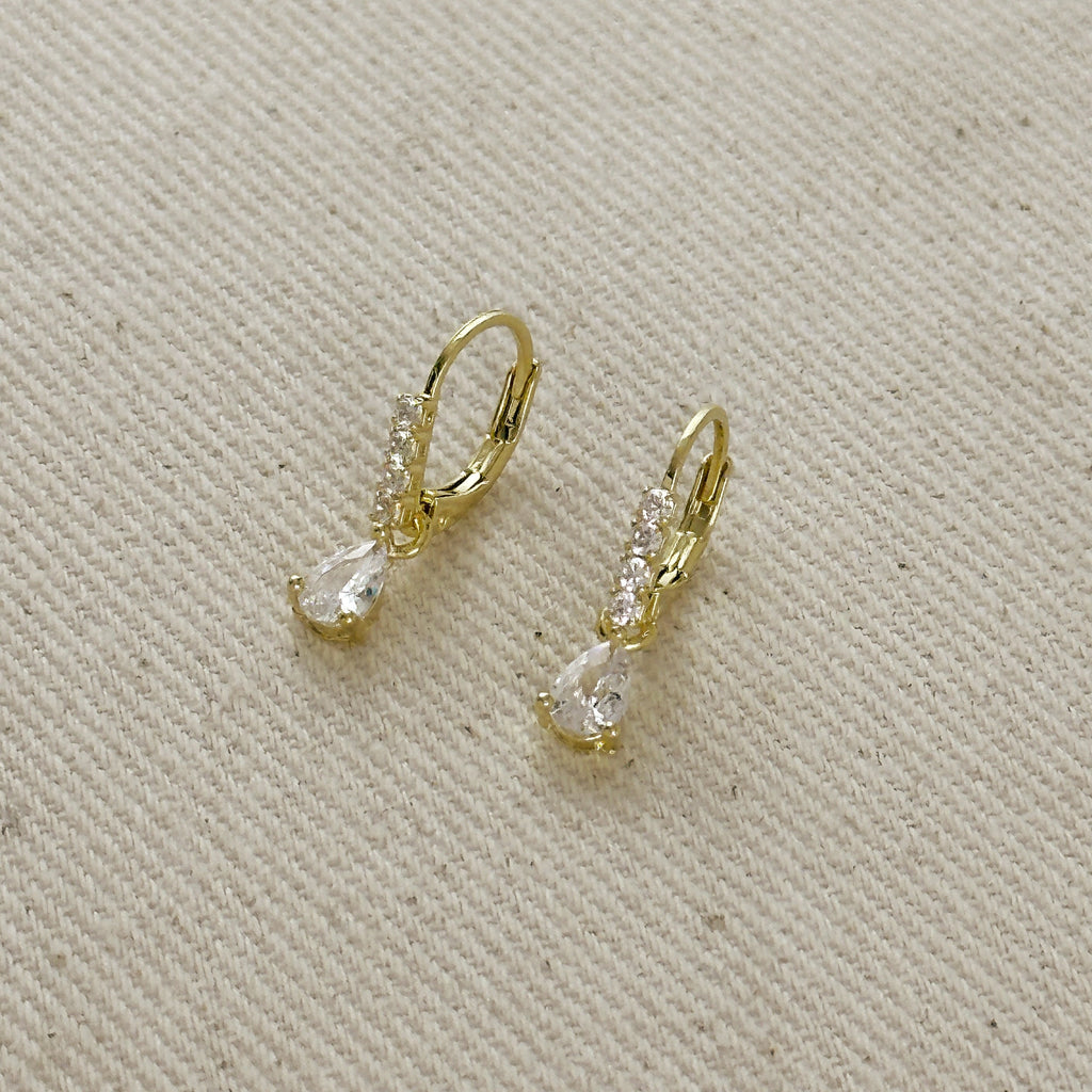 Gold earrings with clear gemstones on a beige fabric background