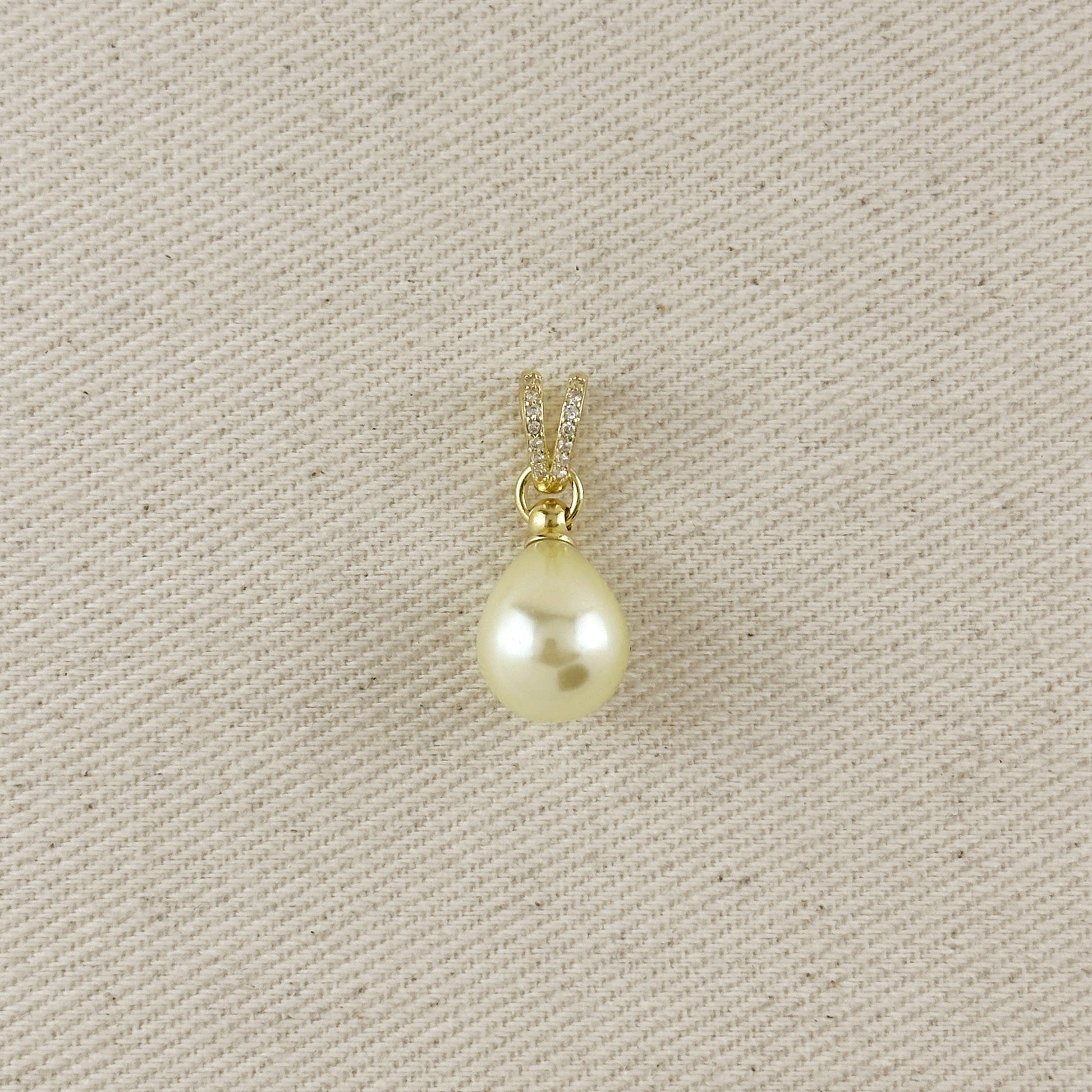 Pearl pendant on a gold chain against a beige fabric background