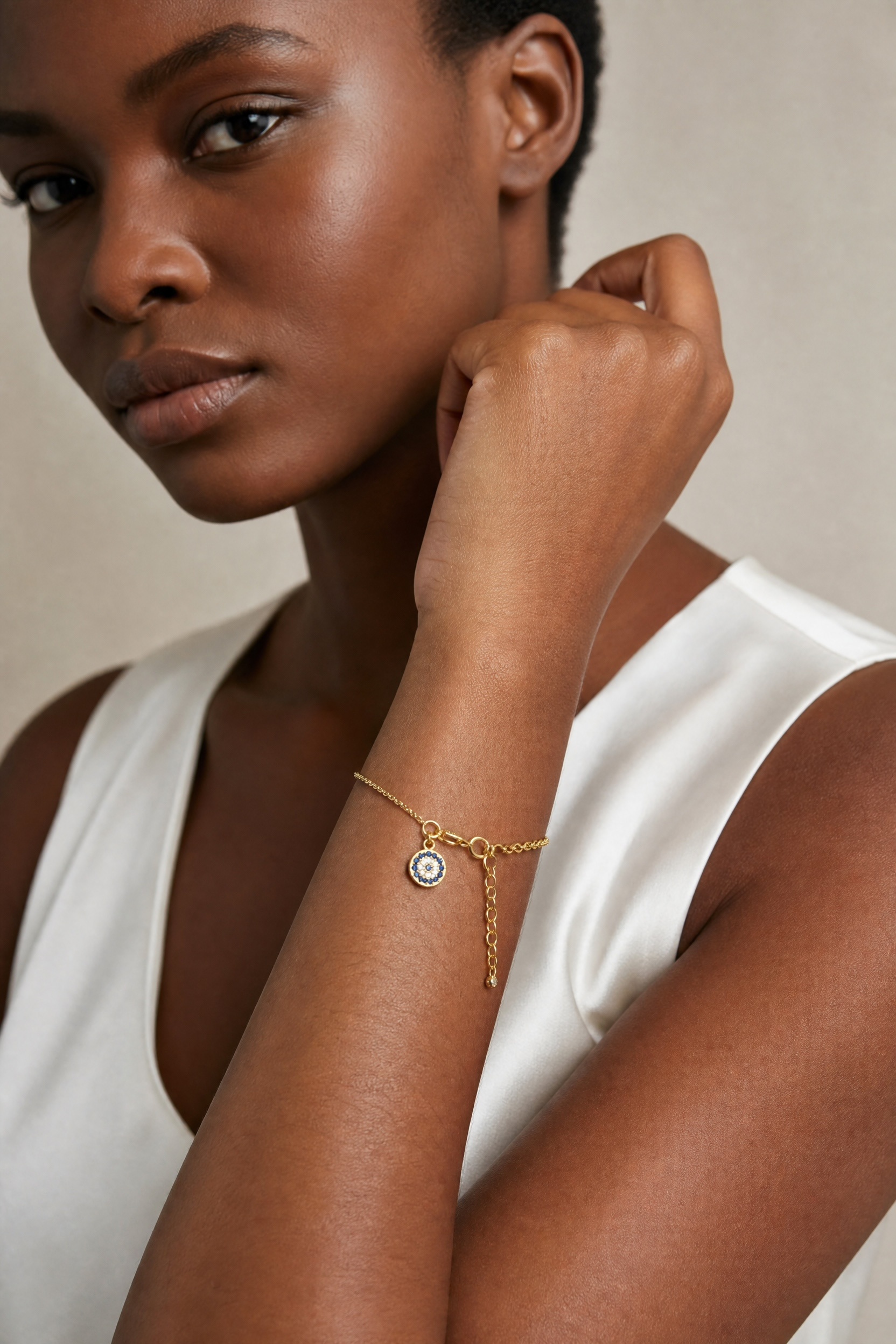 Woman wearing a gold bracelet with a clear stone on a neutral background