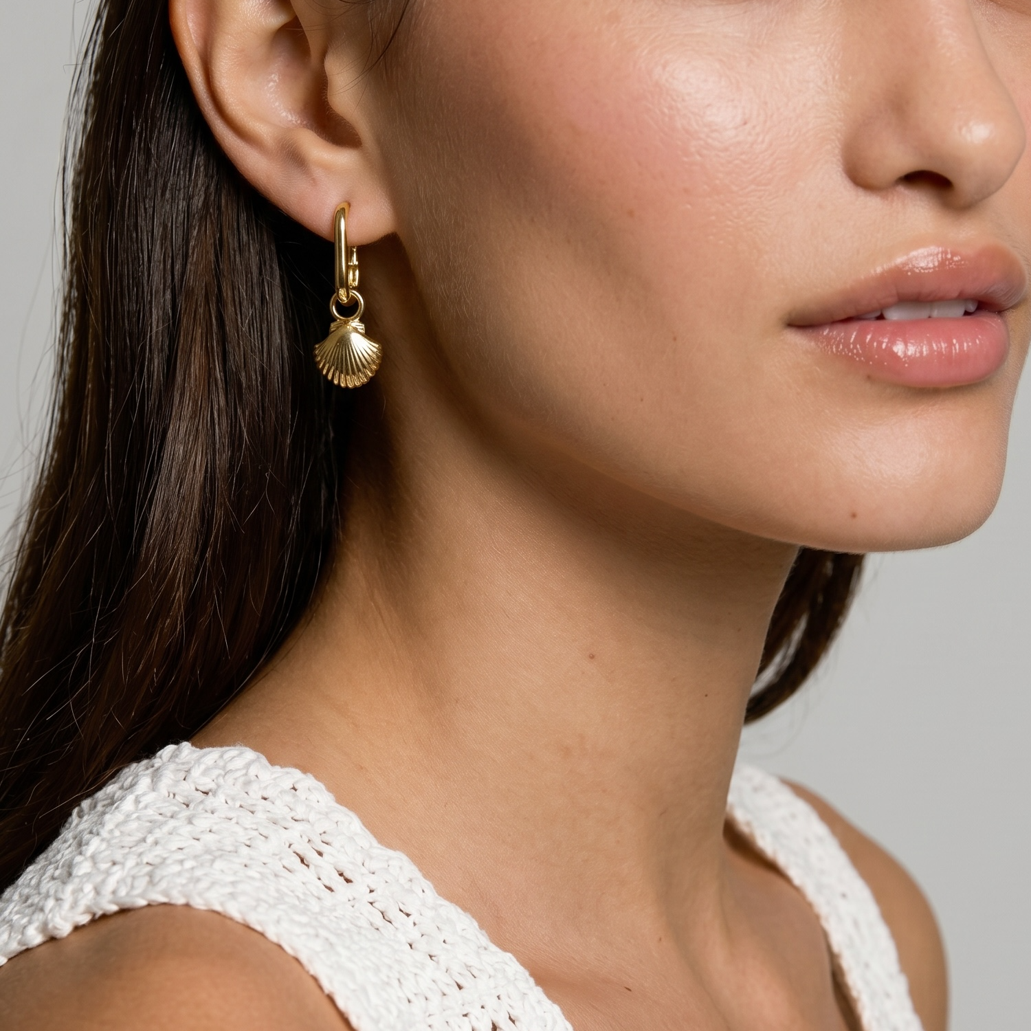 Close-up of a woman wearing gold earrings with a neutral background