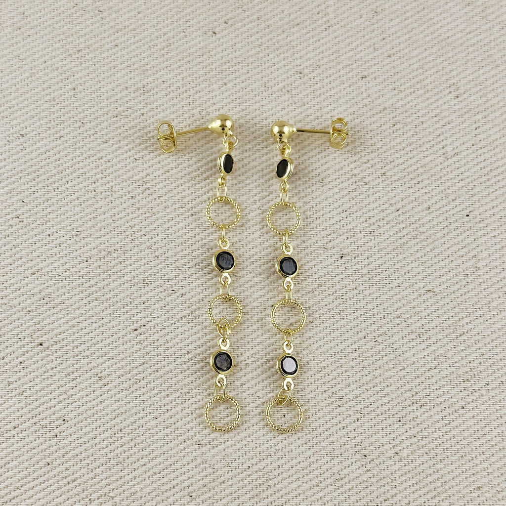 Gold earrings with black stones on a beige fabric background