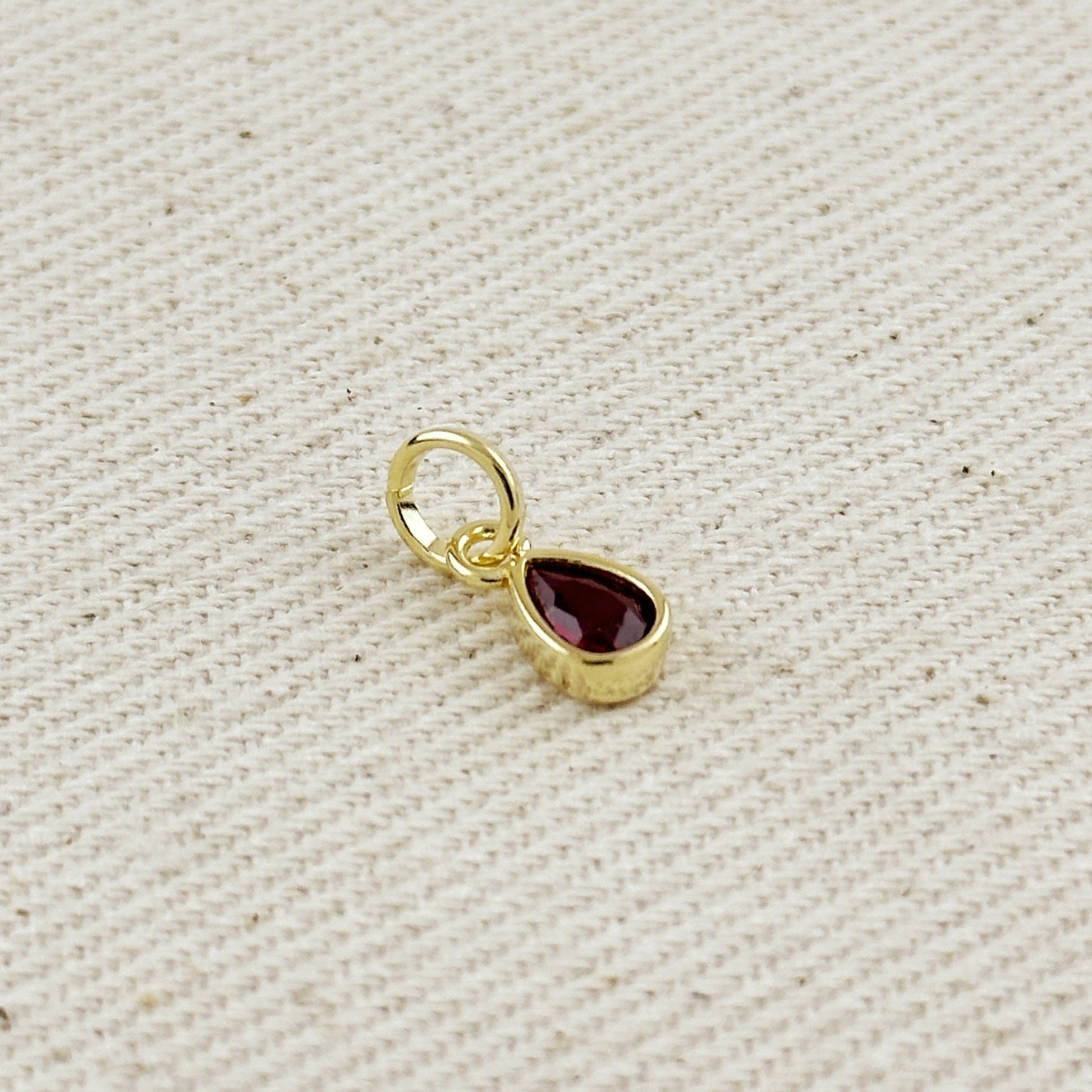 Gold pendant with a red gemstone on a beige fabric background