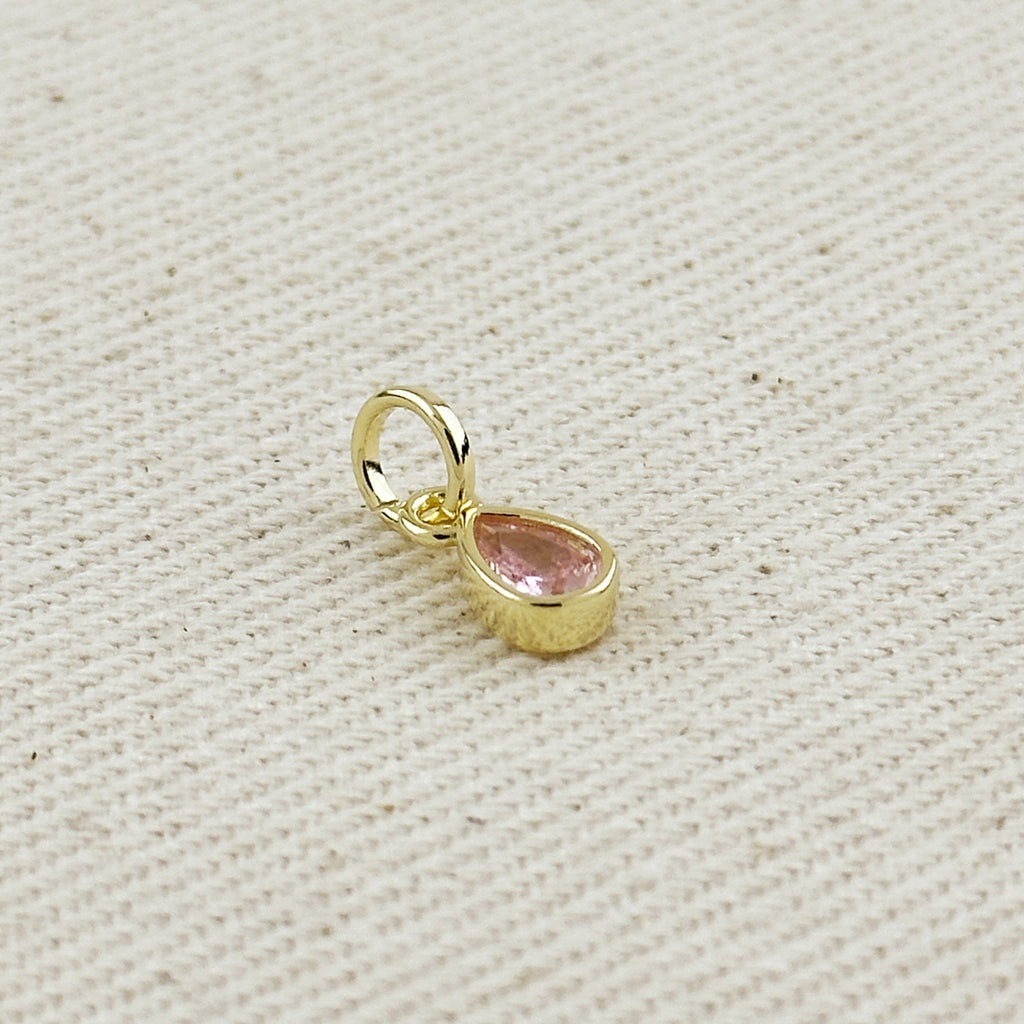 Gold pendant with a pink gemstone on a beige fabric background