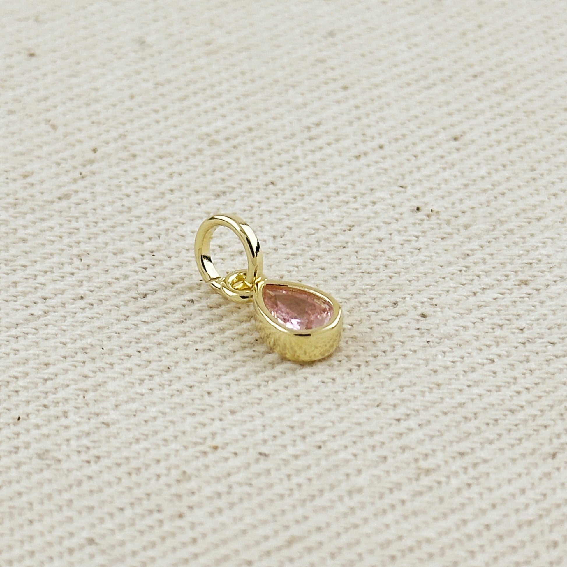 Gold pendant with a pink gemstone on a beige fabric background