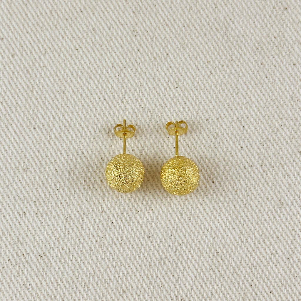Pair of gold earrings on a textured beige surface