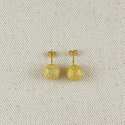 Pair of gold earrings on a textured beige surface