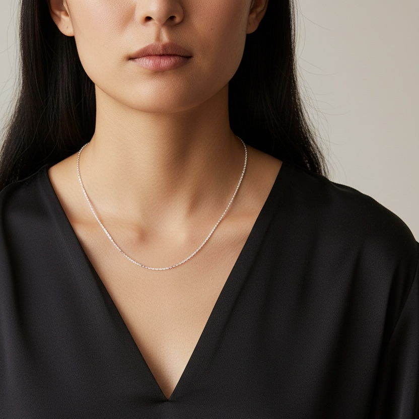 Woman wearing a black top and a delicate necklace against a neutral background