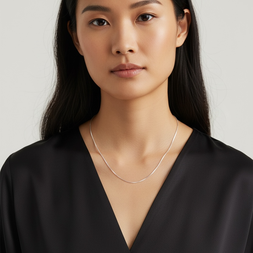 Woman wearing a black top and silver necklace against a plain background