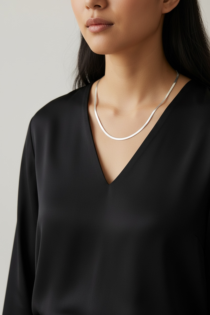 Person wearing a black top and silver necklace against a neutral background