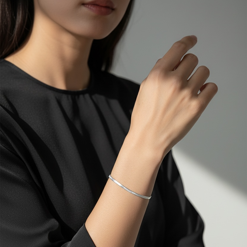 Person wearing a silver bracelet on a plain background