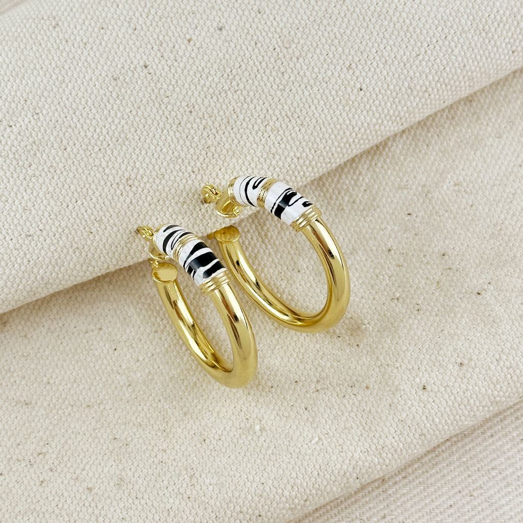 Gold hoop earrings with black and white striped accents on a beige fabric background