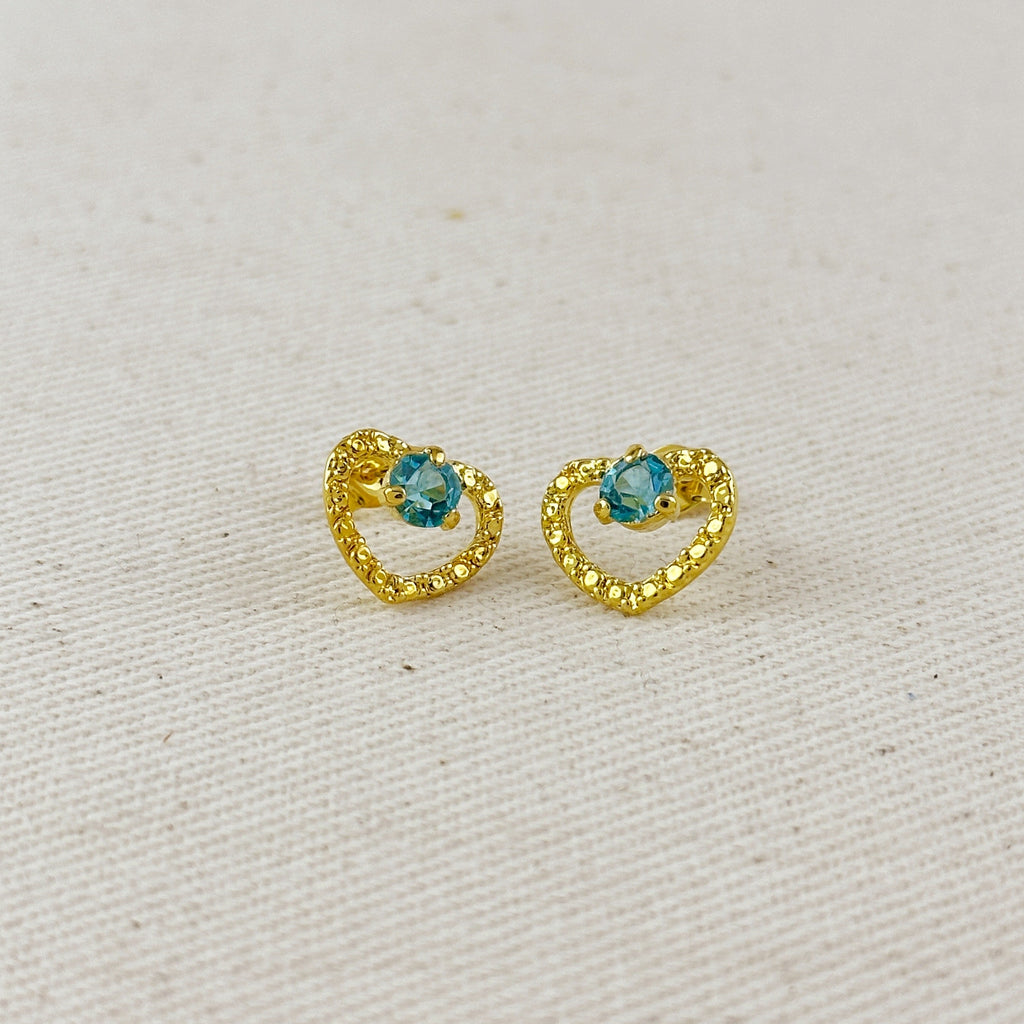 Gold heart-shaped earrings with blue gemstones on a light gray background