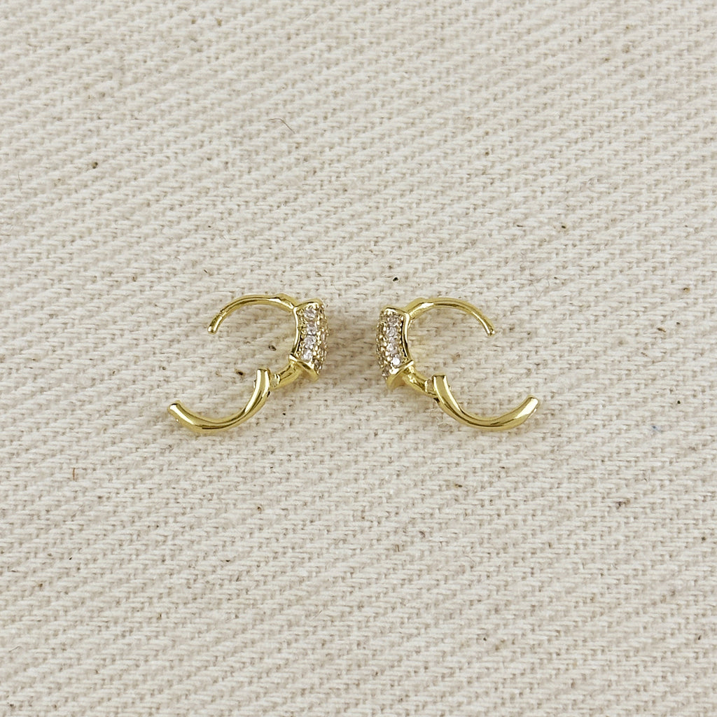 Gold hoop earrings with embedded stones on a beige fabric background
