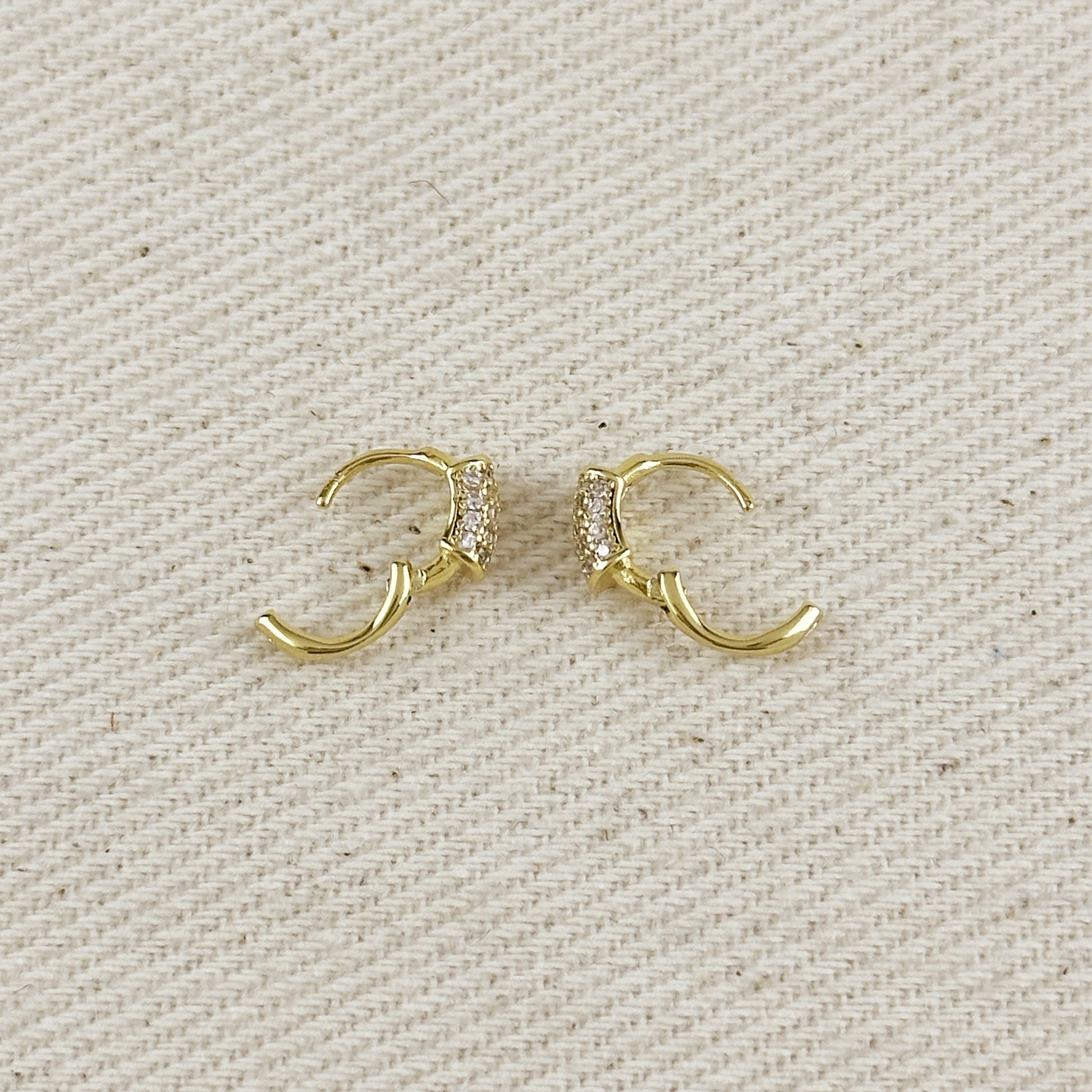 Gold hoop earrings with embedded stones on a beige fabric background