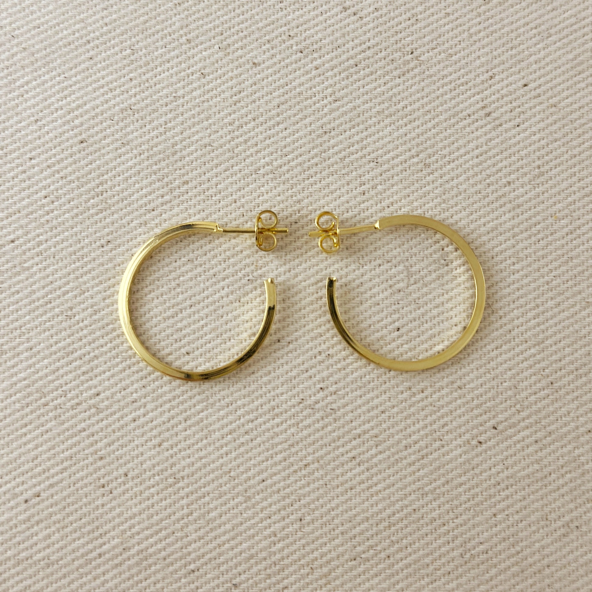 Gold hoop earrings on a beige fabric background