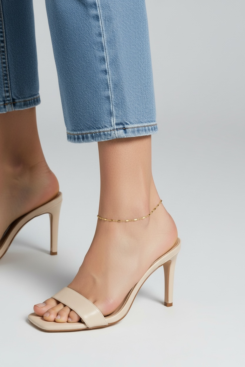 Beige high-heeled sandals worn with blue jeans on a light gray background