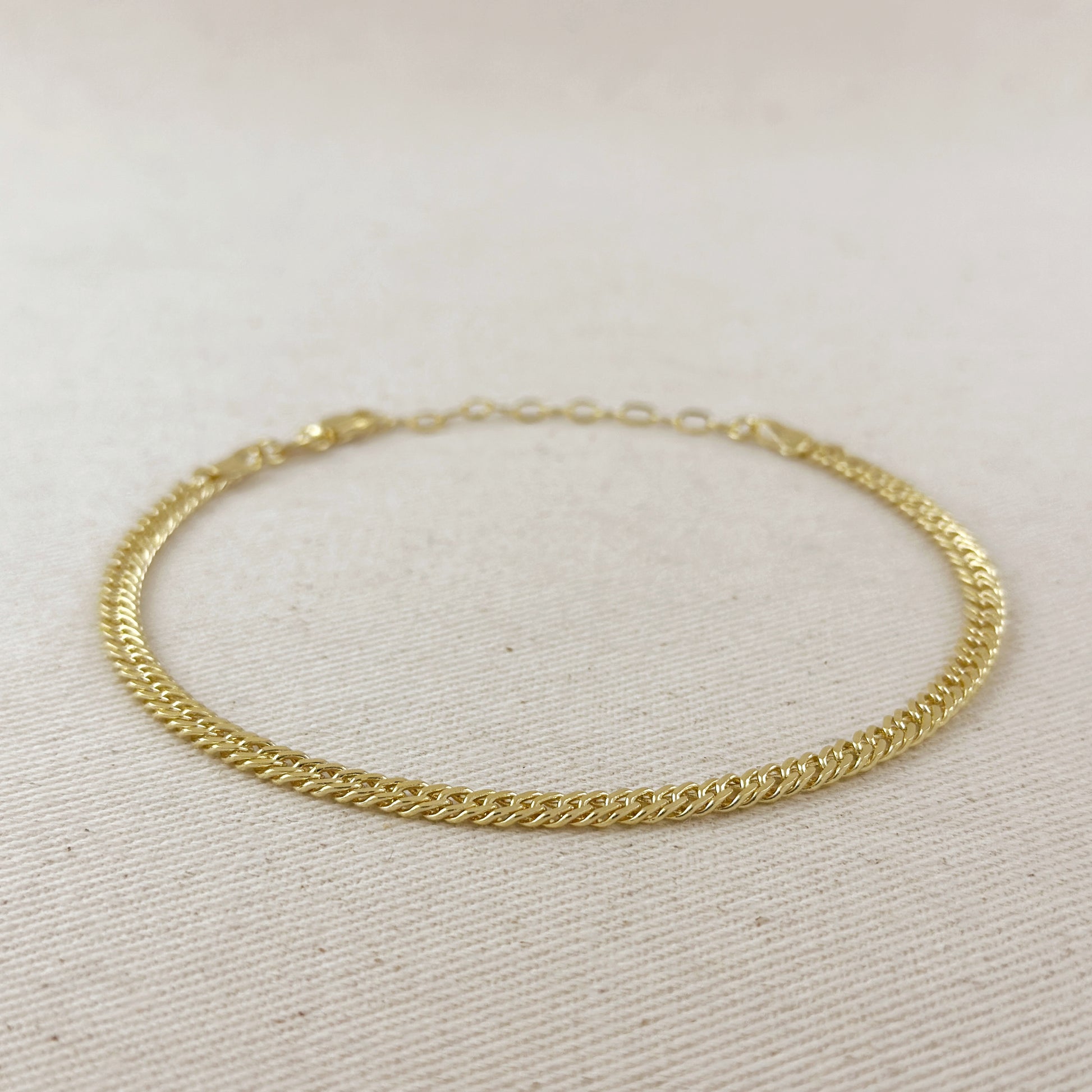 Gold chain bracelet on a light beige fabric background