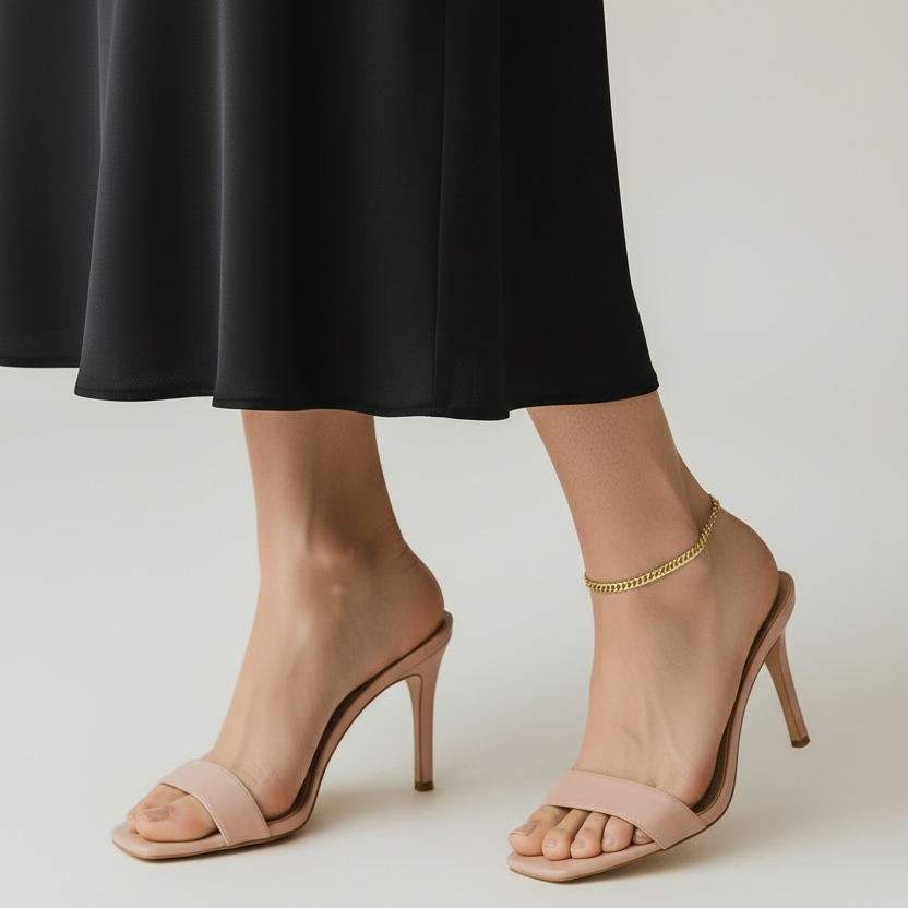 Nude high-heeled sandals worn with a black skirt on a neutral background