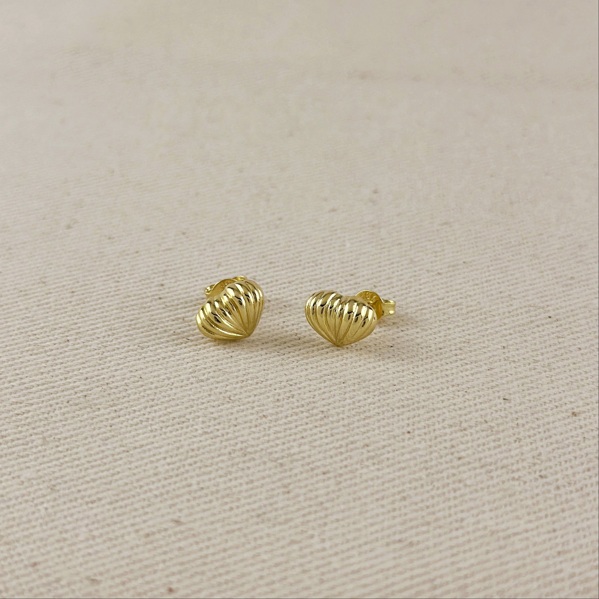 Pair of gold heart-shaped earrings on a beige fabric background