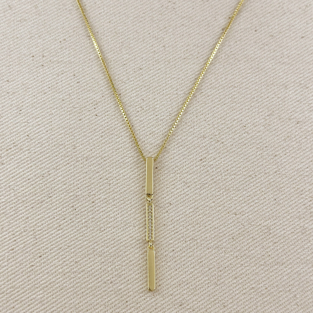 Gold necklace with a vertical pendant on a beige fabric background