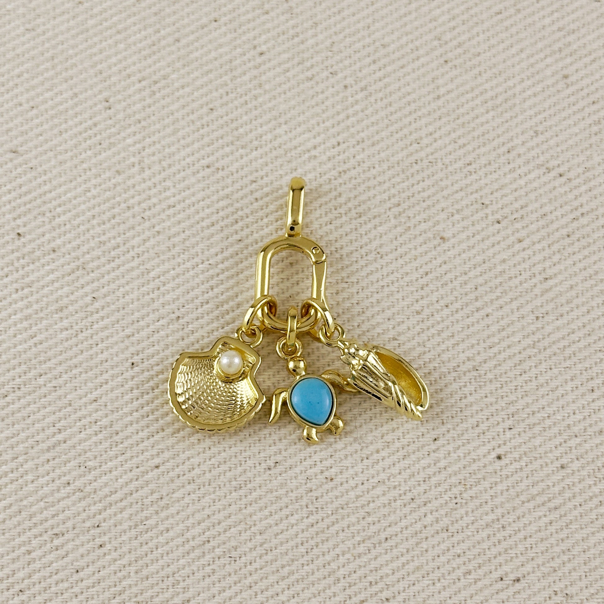 Gold charm with three different charms on a beige fabric background