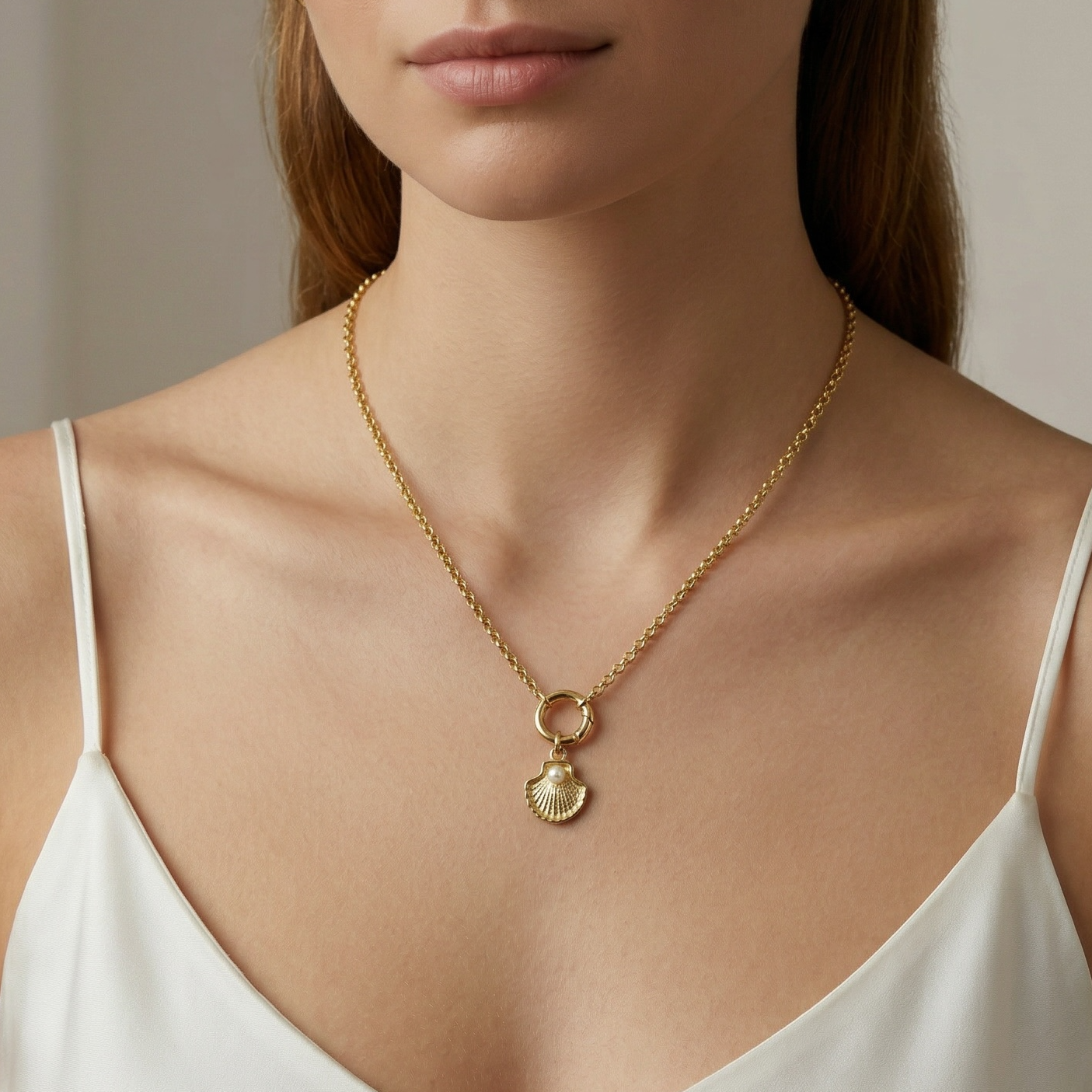 Woman wearing a gold necklace with a shell pendant against a neutral background